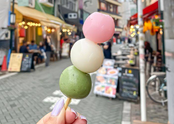 A skewer of dango mochi with a background of a Japanese street.